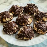 Close-up of freshly baked Schokoladen-Kokos-Makronen, golden-brown coconut macaroons dipped in glossy dark chocolate, arranged on a festive white plate with a holiday-themed background.