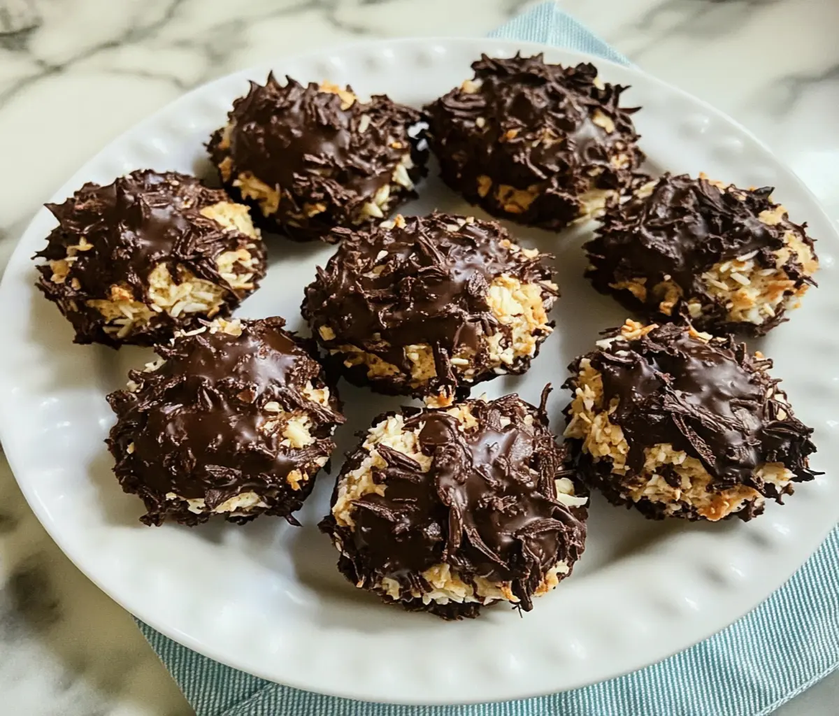 Close-up of freshly baked Schokoladen-Kokos-Makronen, golden-brown coconut macaroons dipped in glossy dark chocolate, arranged on a festive white plate with a holiday-themed background.